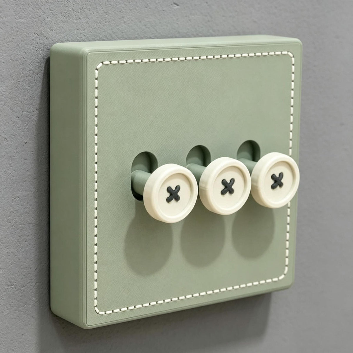 May include: A sage green light switch plate featuring a square shape with white stitched detailing along the border. The plate includes three protruding toggle switches designed to resemble round, cream-colored buttons with black cross-stitch patterns.